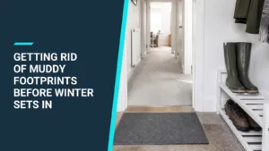 A plain grey doormat inside a front door, with wellies and walking boots on a white shoe rack and a clean, light carpeted hallway beyond.