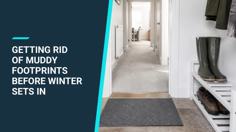A plain grey doormat inside a front door, with wellies and walking boots on a white shoe rack and a clean, light carpeted hallway beyond.